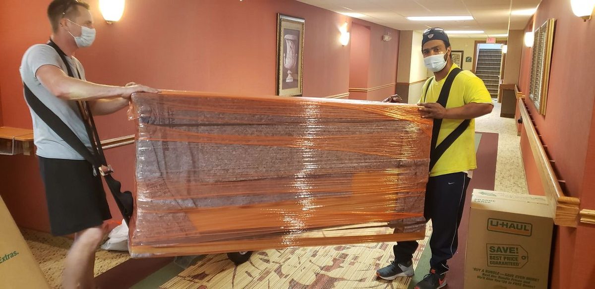 MY Moving Pros crew carrying shrink-wrapped furniture through an Omaha apartment hallway